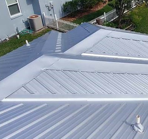 A ribbed metal roof with visible exposed fastener heads along each rib, on a small residential home with a picket fence